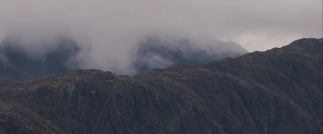 Cloud pours over a dark mountain ridge.