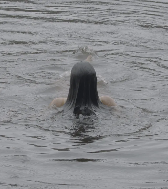 A swimmer's dark hair fans across rippling tarn water.