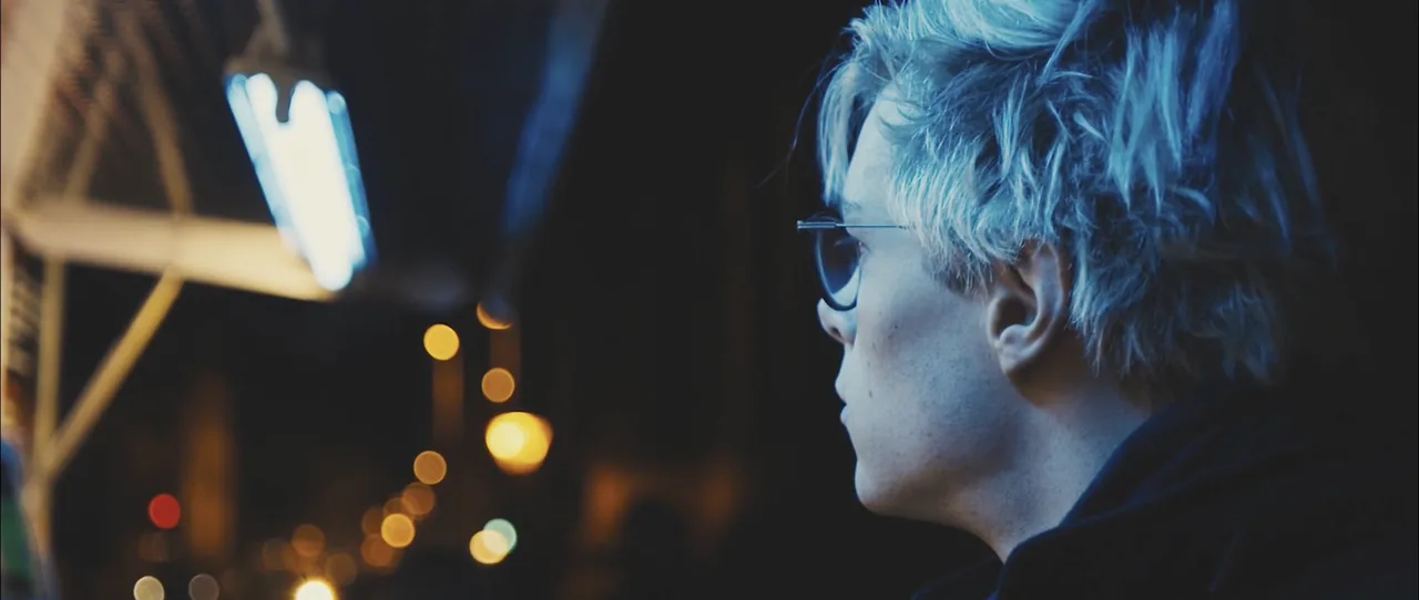 Night still from Insanity: a young man in glasses in profile amid street lights and bokeh.