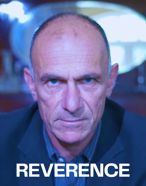 Reverence poster: a close portrait of an older man in blue light with a steady gaze.